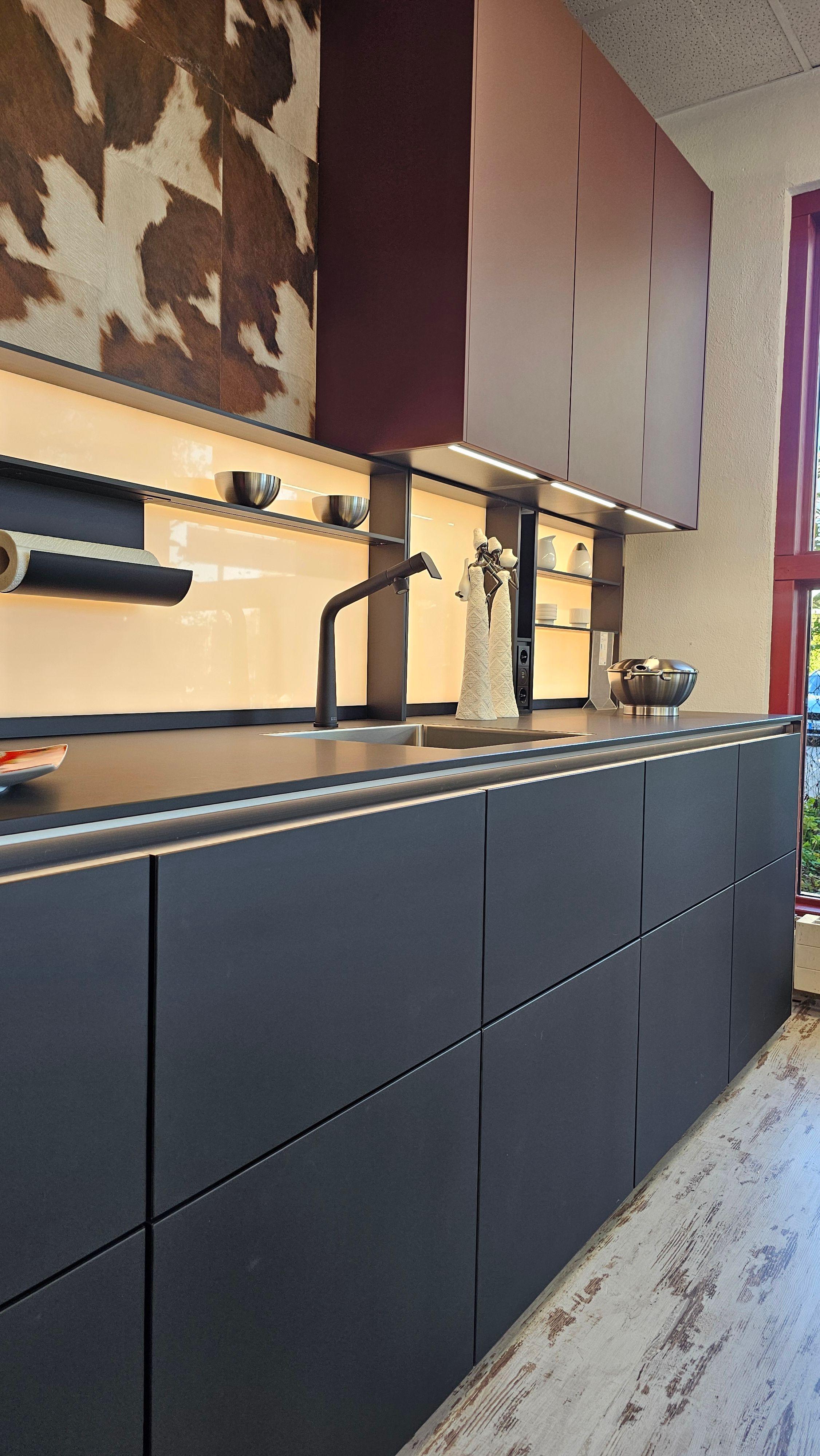 Moderne grifflose Küche mit mattschwarzen Fronten, beleuchtetem Nischenregal und dekorativer Wandverkleidung – stilvolle Küchen in Füssen und dem Allgäu.