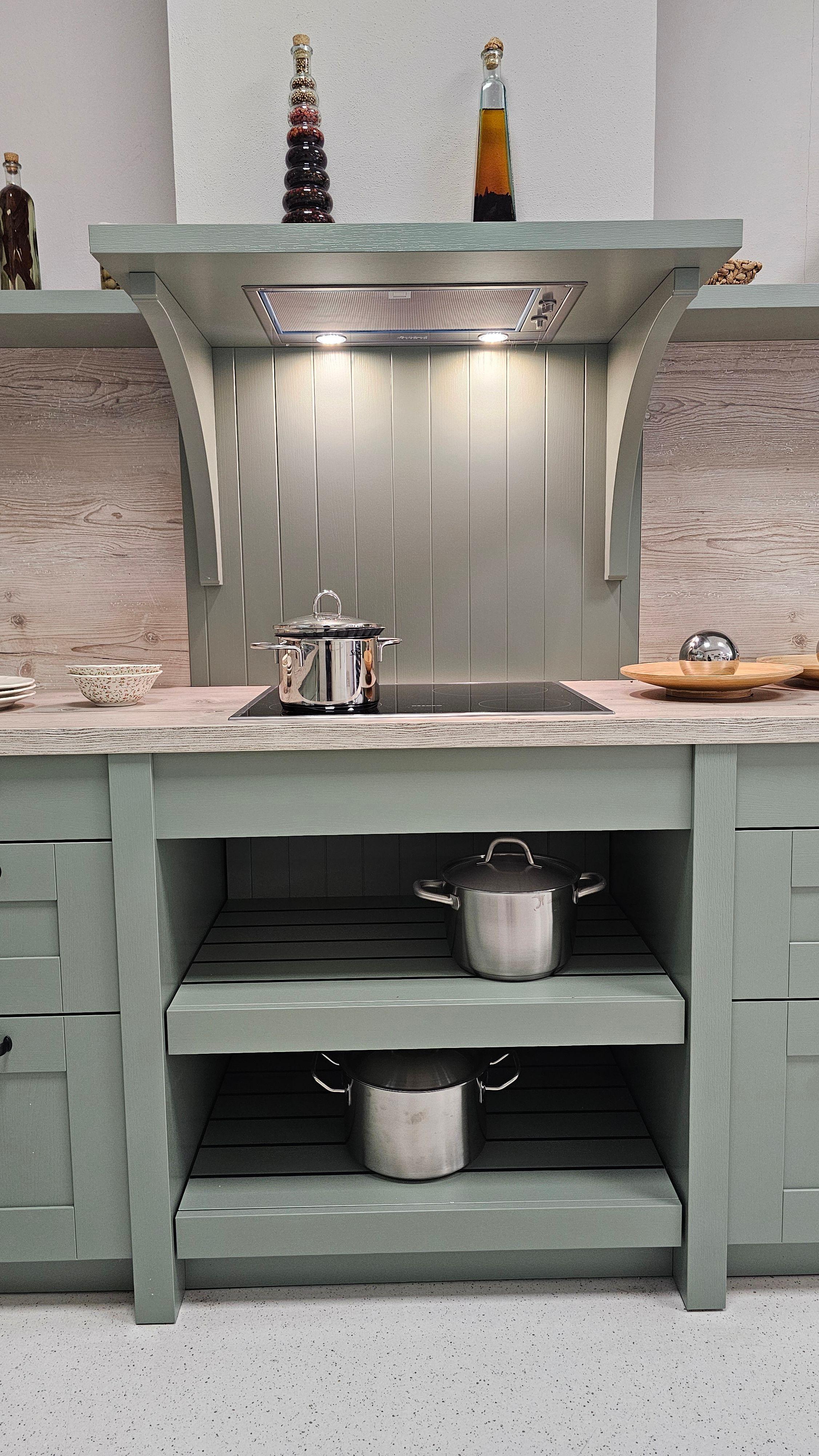 Kochbereich einer grünen Landhausküche mit Induktionsfeld, offenen Regalböden und stimmungsvoller Beleuchtung – hochwertige Küchen in Füssen und dem Allgäu.