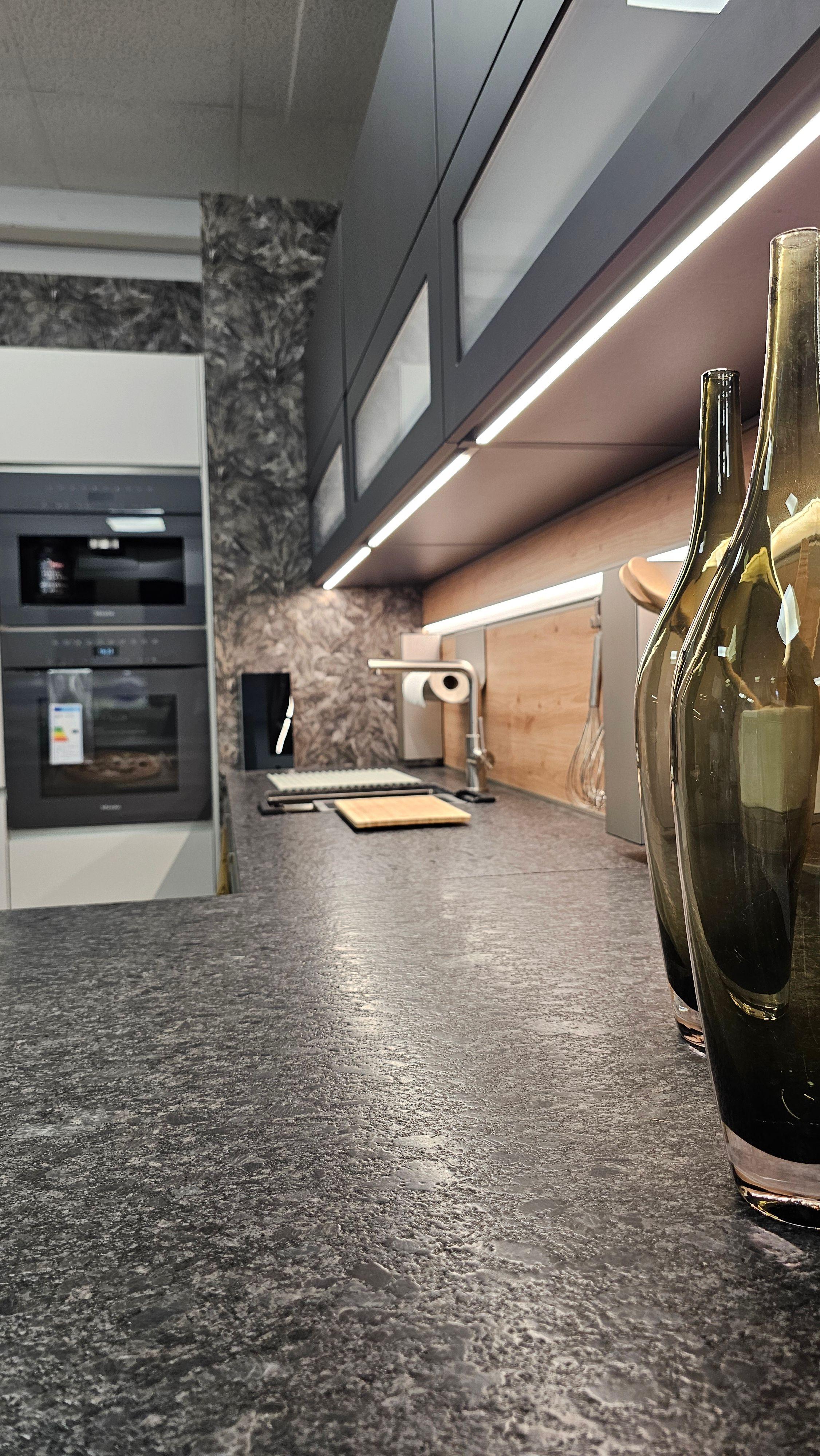 Küchenarbeitsplatte in Steinoptik mit Glasvasen, dahinter Gerätewand und Nischenrückwand – elegante Küchen in Füssen und dem Allgäu.