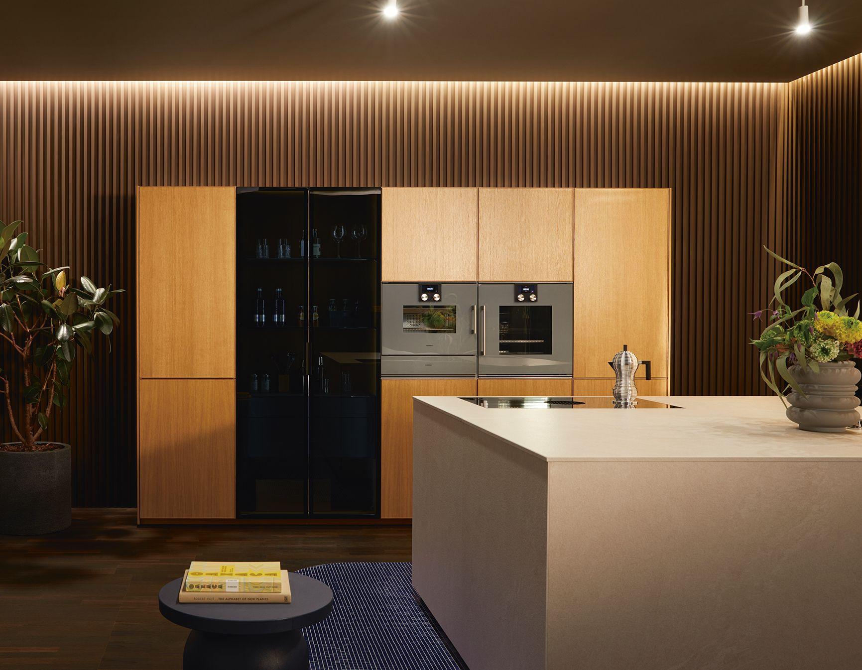 Moderne grifflose Küche in warmem Holzton mit Kochinsel, eingebauten Backöfen und stilvoller Beleuchtung – hochwertige Küchenplanung Allgäu mit elegantem Design und viel Stauraum.