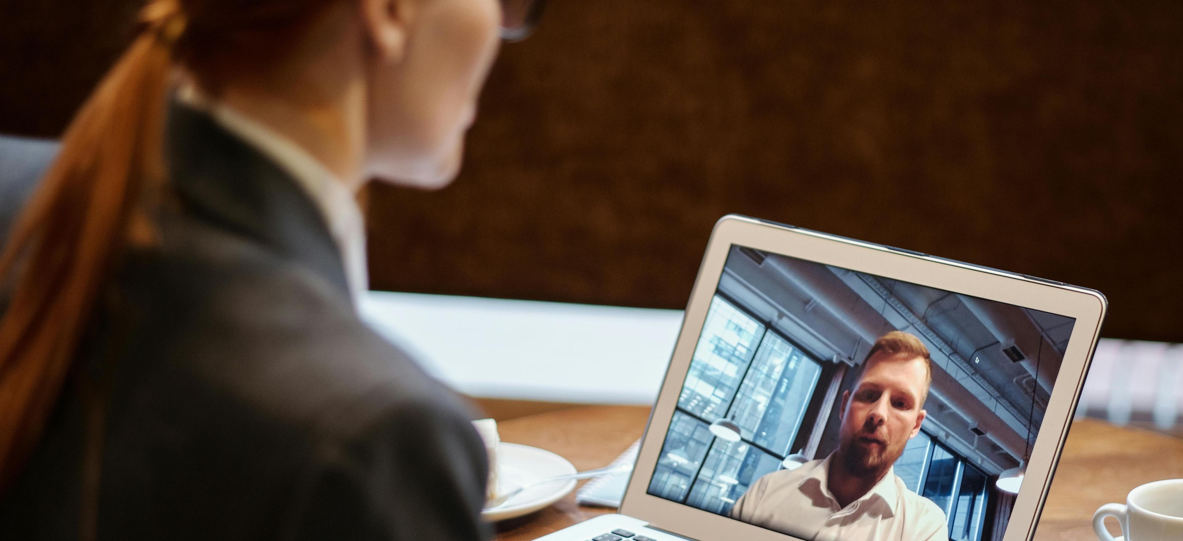 Eine junge Frau sitzt vor Ihrem Notebook und unterhält sich via Video-Call mit einem Küchenplaner.