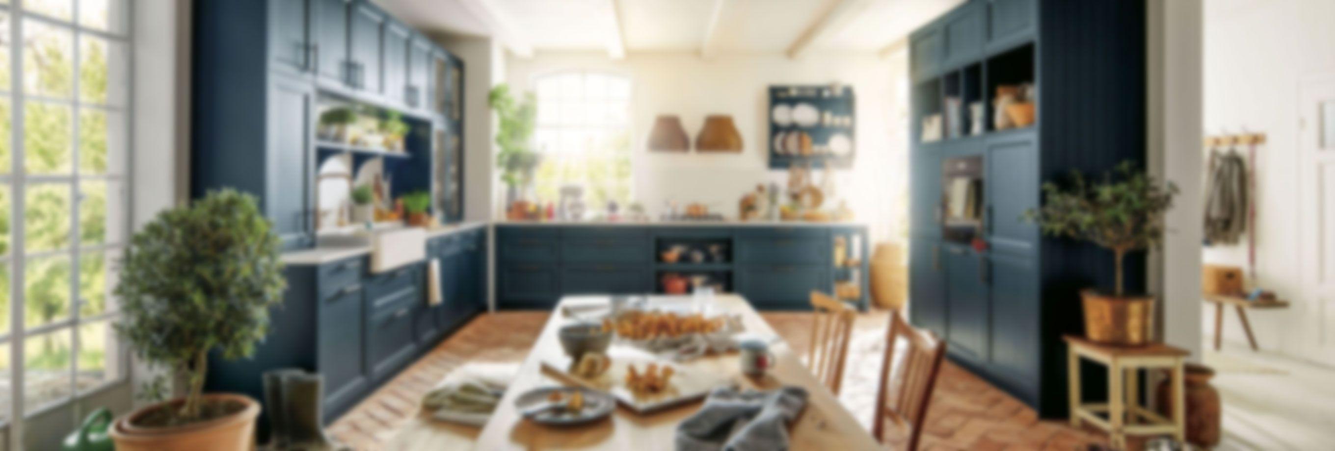 Gemütliche Landhausküche in tiefblau mit großem Esstisch, offenen Regalen und natürlichem Tageslicht – individuelle Küche renovieren im Allgäu für warmes Wohngefühl und viel Stauraum.